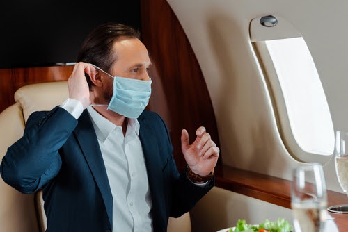 Selective focus of businessman putting on medical mask near champagne and salad on table in airplane