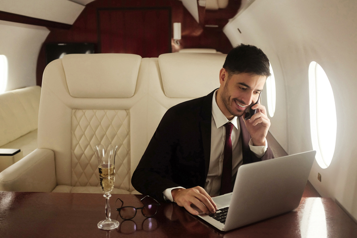 Billionaire or rich businessman flying first class and working on plane with laptop and glass of champagne. Private jet