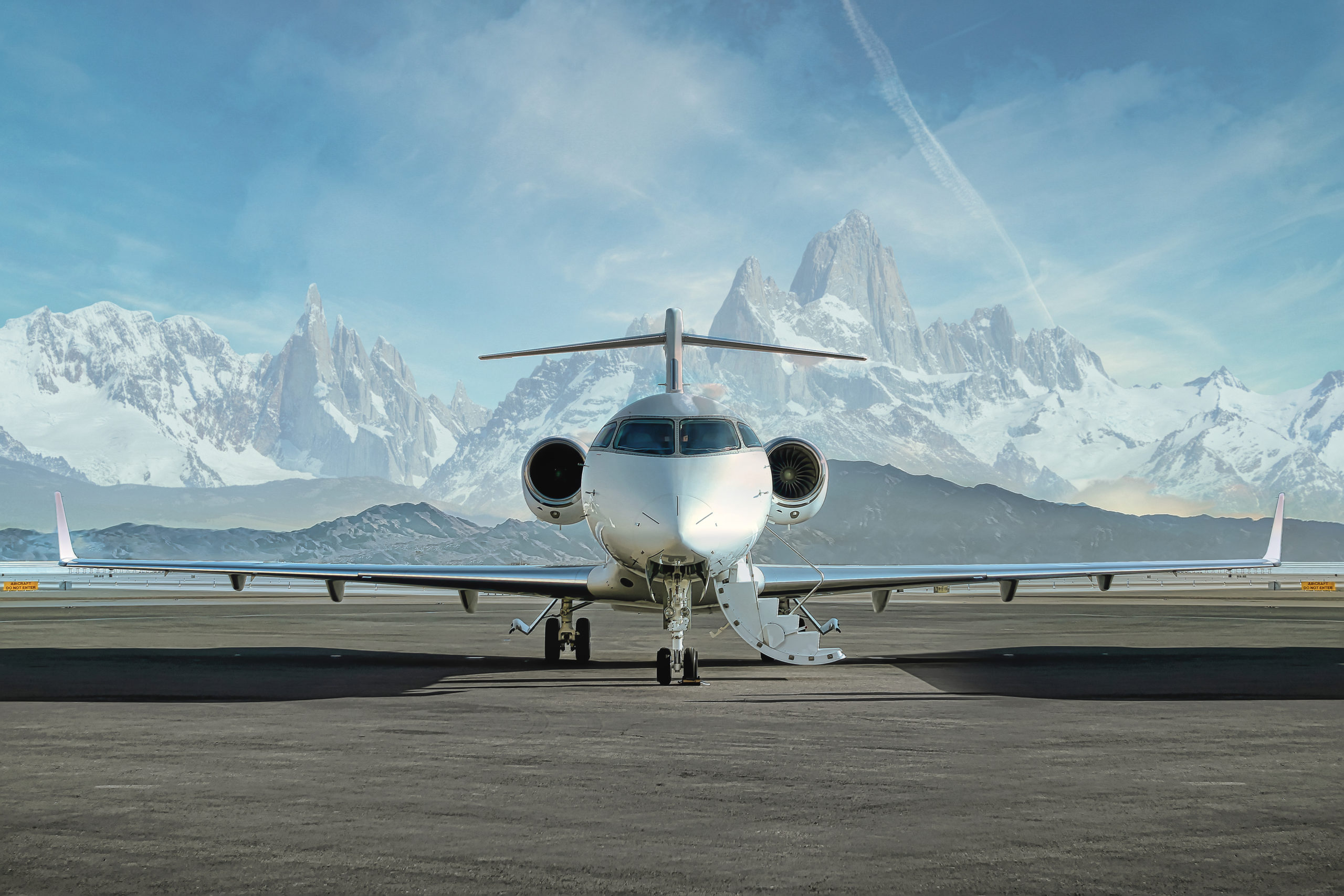 Head on photo of a private jet waiting on runway to be boarded with snowy mountains in the background